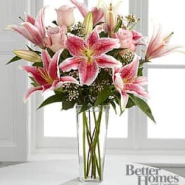 Tall glass vase of pink lilies and pale pink roses in a vertical bouquet
