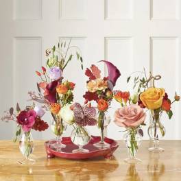 Five small floral arrangements in clear glass vases on a red tray