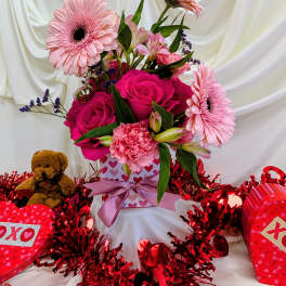Pink roses and gerbera daisies in a heart-patterned gift box with a teddy bear