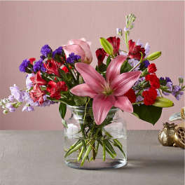 Mixed bouquet with pink lilies, roses, and red and purple blooms in a glass vase