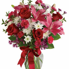 Bouquet of red roses, pink lilies, and white daisies in a glass vase with a red ribbon