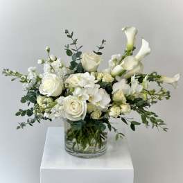 White roses, orchids, and calla lilies arranged in a clear glass cylinder vase