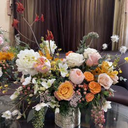 Large mixed bouquet of peach, white, and orange flowers in a metallic vase
