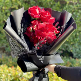 Hand-held bouquet of bright red roses wrapped in matte black paper with black mesh accents
