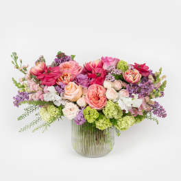 Low arrangement of pink, peach, and purple flowers in a ribbed clear glass vase