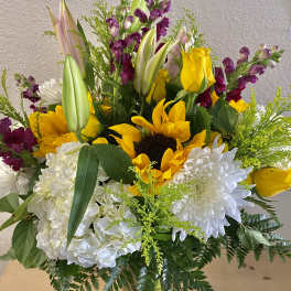 Bouquet of sunflowers, white chrysanthemums, and purple snapdragons in a glass vase