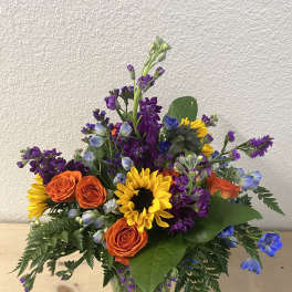 Mixed bouquet with sunflowers, orange roses, and purple flowers in a glass vase