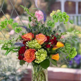 Mixed bouquet of roses and green blooms in a clear glass vase