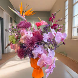 Colorful bouquet in an orange vase with orchids and tropical blooms