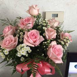 Pink roses with small white daisies in a vase tied with a pink ribbon.