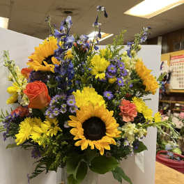 Mixed bouquet with sunflowers, roses, and purple flowers in a tall vase