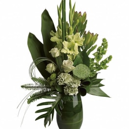 Green floral arrangement in a glass vase with white blooms and tropical leaves
