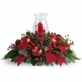 Red candle in a glass hurricane surrounded by apples, pinecones, and ribbon