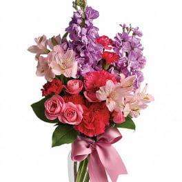 Bouquet of pink and purple flowers in a clear glass vase with a pink ribbon