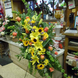 Large standing floral spray with yellow lilies, sunflowers, and orange roses