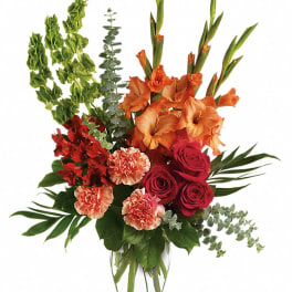 Bouquet of orange gladiolus, red roses, and carnations in a clear glass vase