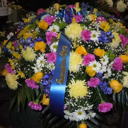 Large funeral spray with mixed yellow, pink, white, and blue flowers