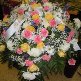 Large funeral spray with yellow roses, pink carnations, and white daisies