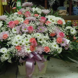 Large pastel floral arrangement in a basket with a lavender ribbon