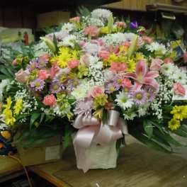 Large mixed flower arrangement in a white basket with a pink ribbon