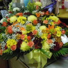 Large mixed flower arrangement in a white container with a green ribbon
