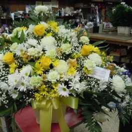 Large yellow and white floral arrangement with a ribboned container