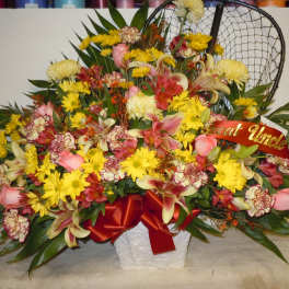 Large mixed flower arrangement in a white basket with a red ribbon