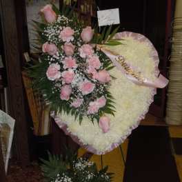 Pink roses and carnations on a white standing floral wreath with a pink ribbon