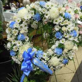 Heart-shaped floral wreath with white and blue flowers on a stand