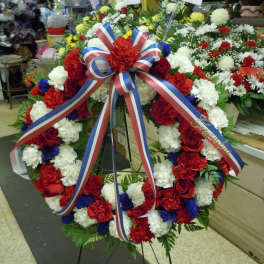 Large red, white, and blue funeral wreath on a stand with ribbon