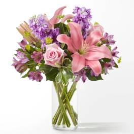 Pink lilies and purple flowers in a clear glass vase