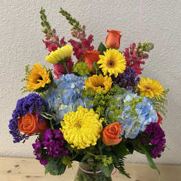 Colorful mixed bouquet in a glass vase with roses, hydrangeas, and daisies