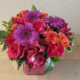 Pink and purple mixed flower arrangement in a square pink vase
