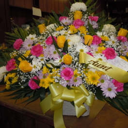 Large mixed flower arrangement with yellow ribbon in a white container