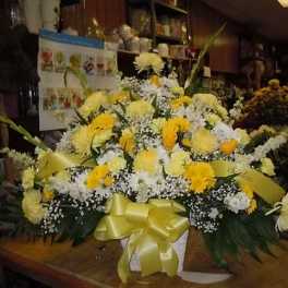 Yellow and white floral arrangement in a white basket with a yellow ribbon
