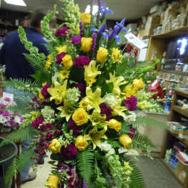 Tall floral spray with yellow roses and lilies in yellow, purple, and green