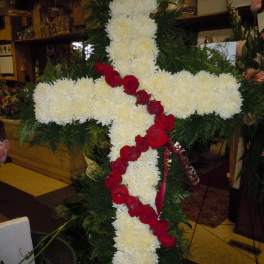 White floral cross with red roses draped diagonally across it