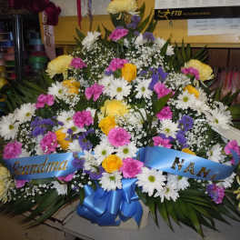 Large floral spray with white daisies, yellow roses, pink carnations, and blue ribbon