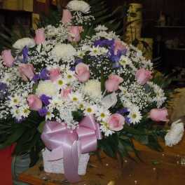 Large floral arrangement with pink roses, white daisies, and purple accents in a white container
