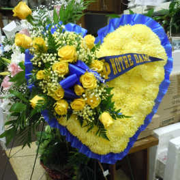 Heart-shaped yellow floral tribute with blue ribbon and yellow roses