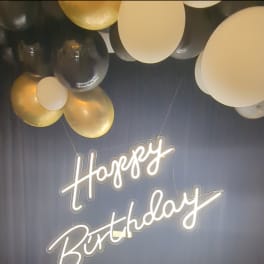 Birthday sign with gold, black, and white balloons overhead