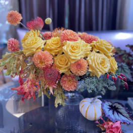 Yellow roses and peach dahlias in a low arrangement with autumn leaves