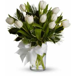 Arrangement of white tulips with variegated foliage in a clear glass vase tied with a white bow.