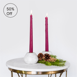 Pair of tall burgundy taper candles in white holders on a round marble table
