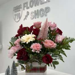 Pink and red floral arrangement in a square vase with plaid ribbon