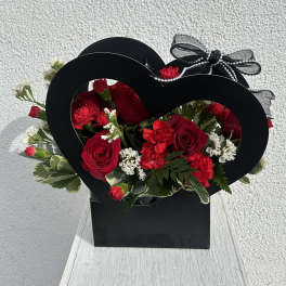 Red roses and carnations in a black heart-shaped box with a ribbon bow