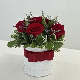 Red roses arranged in a white hat box with a red ribbon