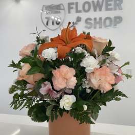 Bouquet of orange lilies, peach and white flowers in a tan vase