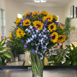 Sunflower bouquet with purple daisies in a clear glass vase and plaid ribbon