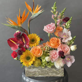 Mixed floral arrangement with sunflowers, roses, orchids, and bird-of-paradise in a wooden box